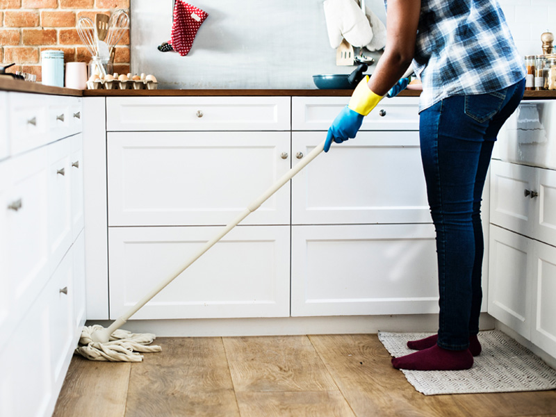 A person in the kitchen cleaning with a mop.