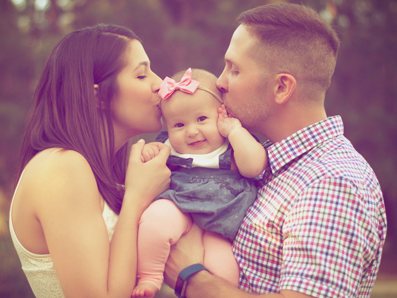 A man and woman kissing their baby girl.